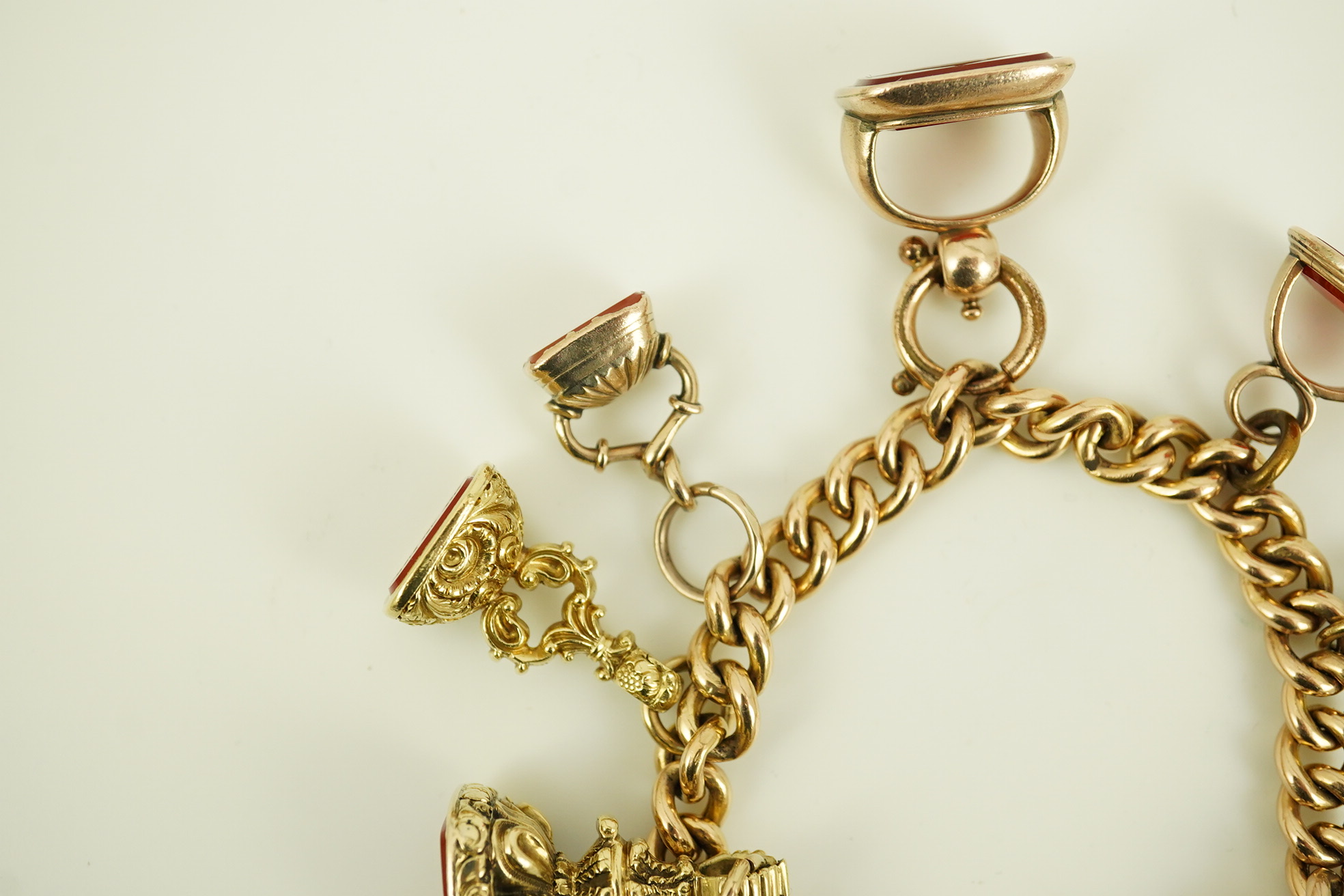 An Edwardian 15ct gold curb link charm bracelet with heart shaped padlock clasp, hung with six assorted gold overlaid and carnelian set fob seals